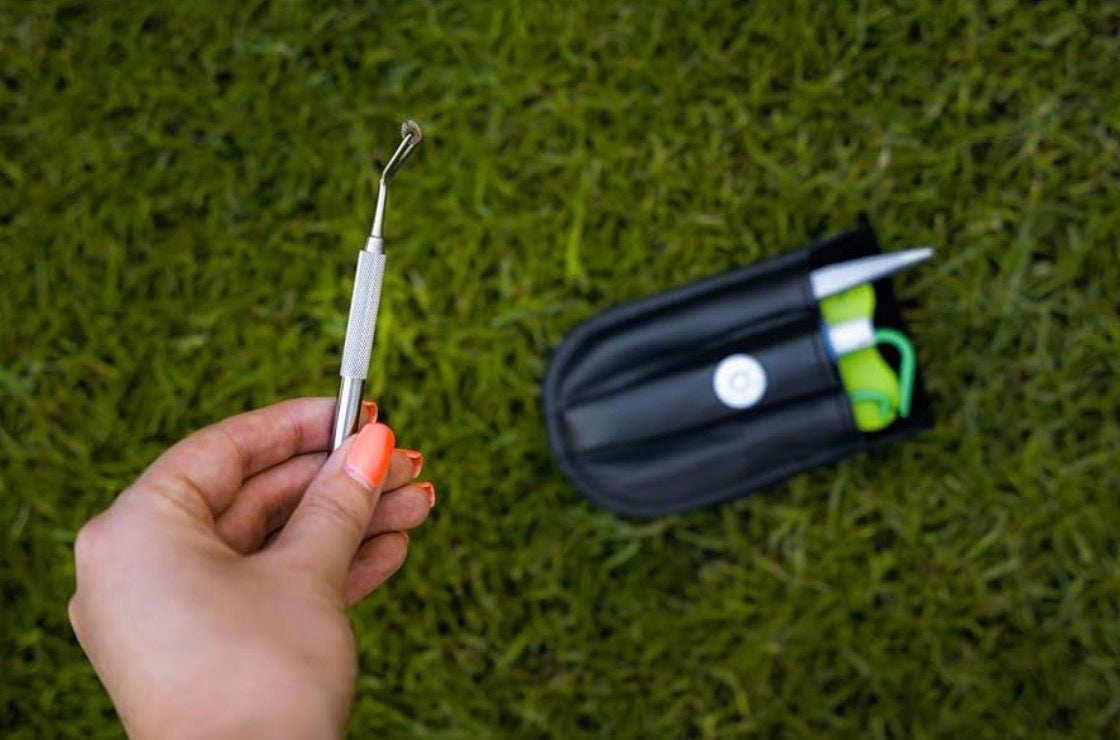Hand holding a fishing hook with a black case on grass
