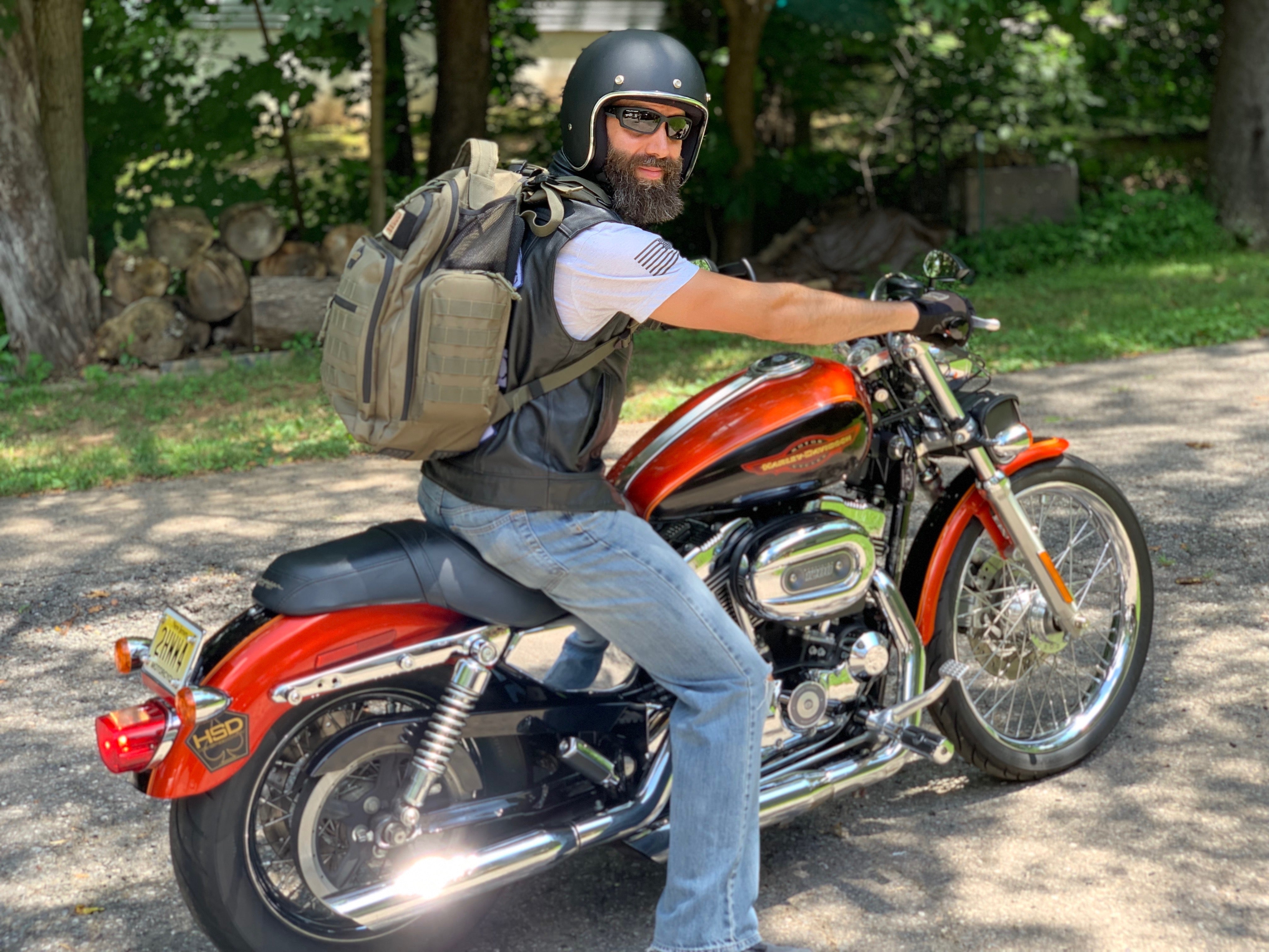 Man with a beard wearing a helmet and backpack sitting on a red motorcycle.