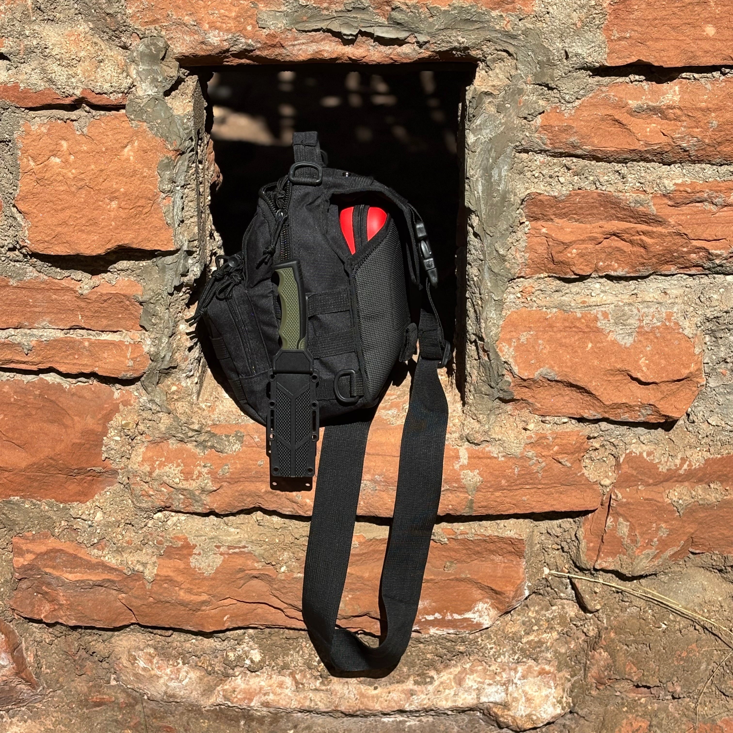 Black tactical backpack with red accents hanging from a stone wall.