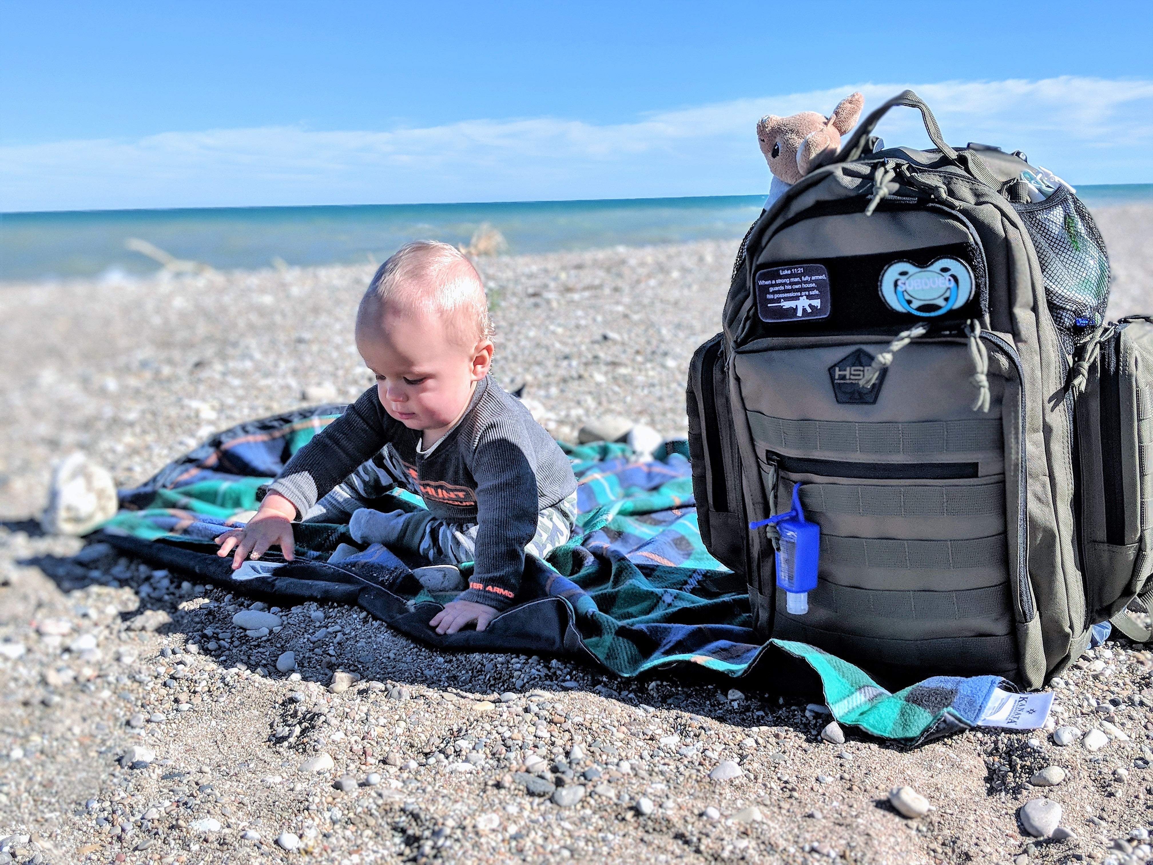 Child playing on a beach with a backpack and water bottle nearby