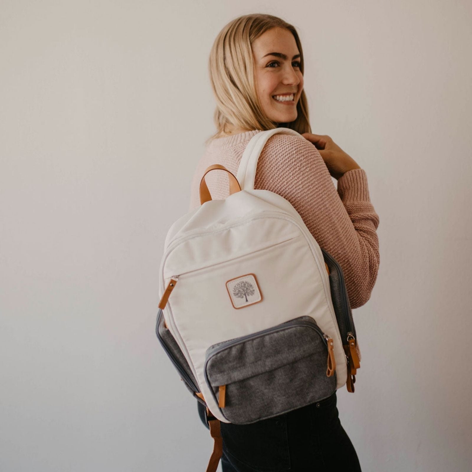 Woman wearing a white backpack with a visible brand logo against a plain background