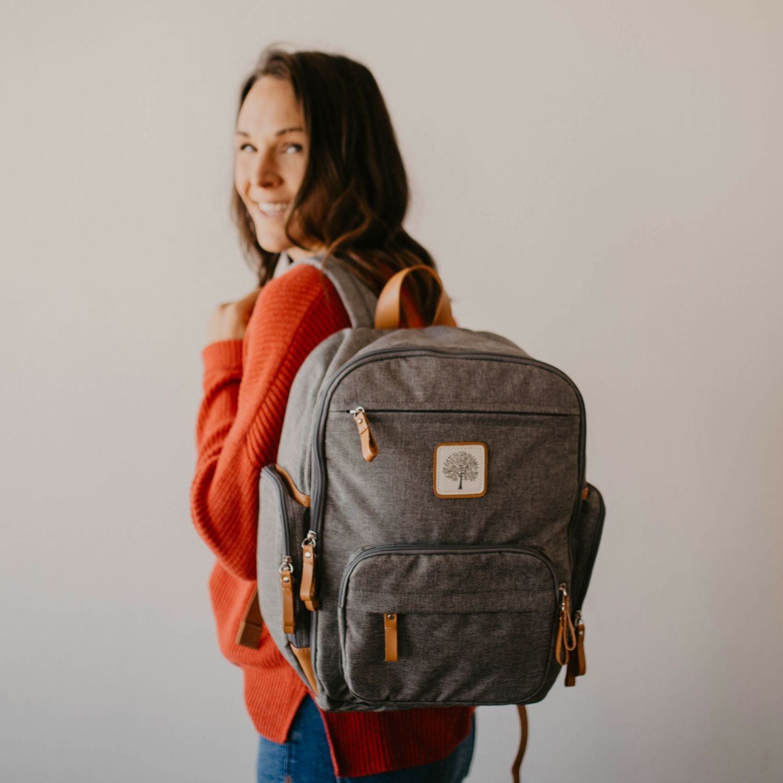 Person wearing a gray backpack with a visible brand logo on a plain background