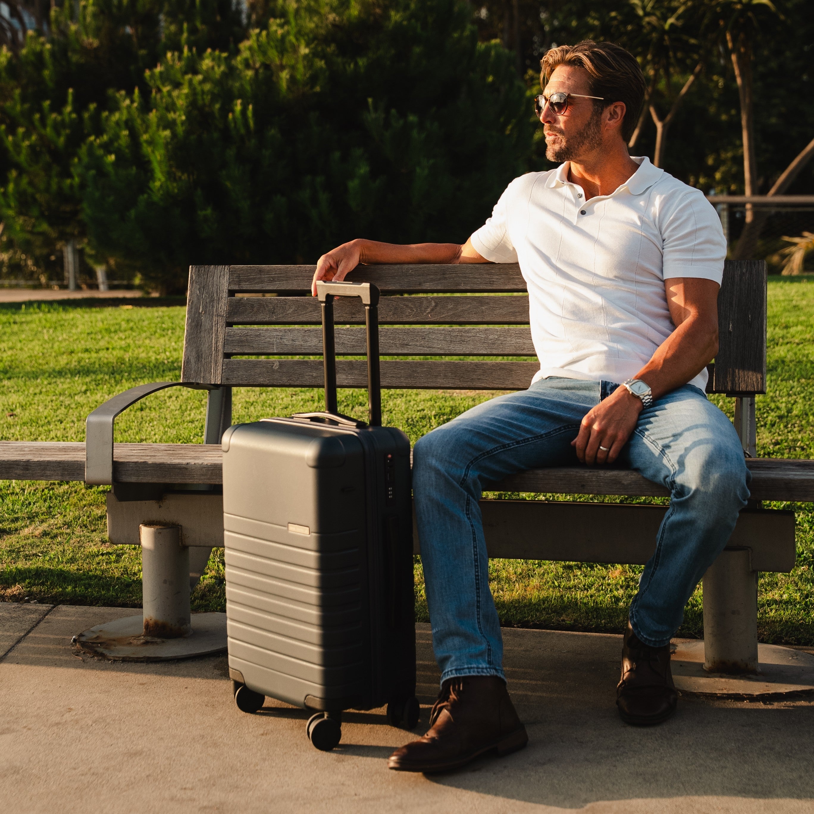Man sitting on a bench with a suitcase next to him in a park setting