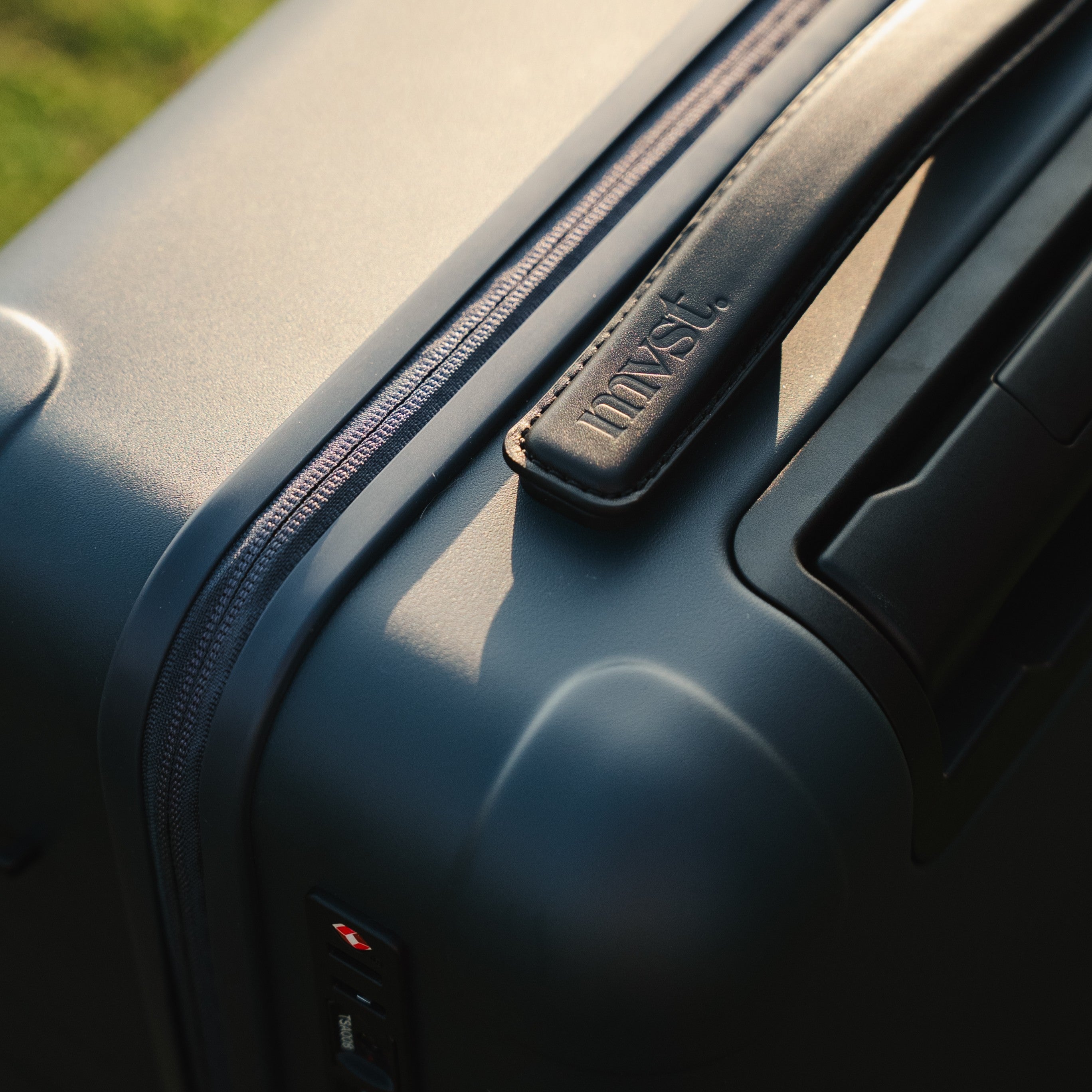 Close-up of a black suitcase with a brand logo on a blurred natural background