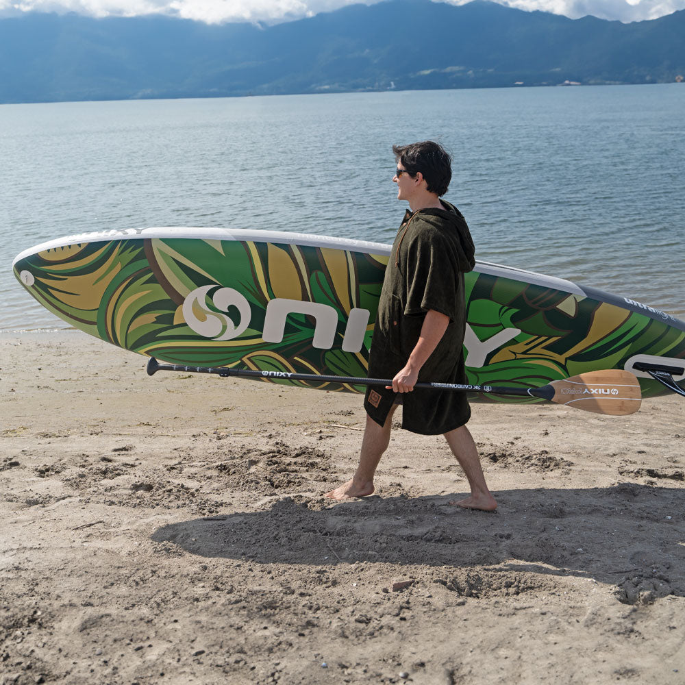 Person walking on a beach with a green and yellow paddleboard
