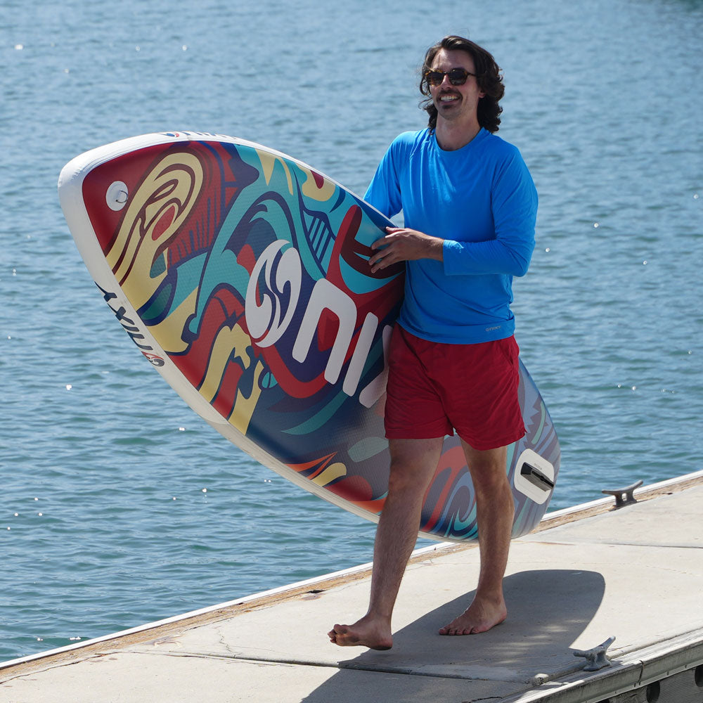 Man holding a colorful surfboard with water in the background