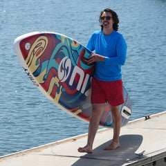 Man holding a colorful surfboard with water in the background