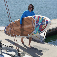 Person holding a colorful surfboard with 'SIXXY' branding near water
