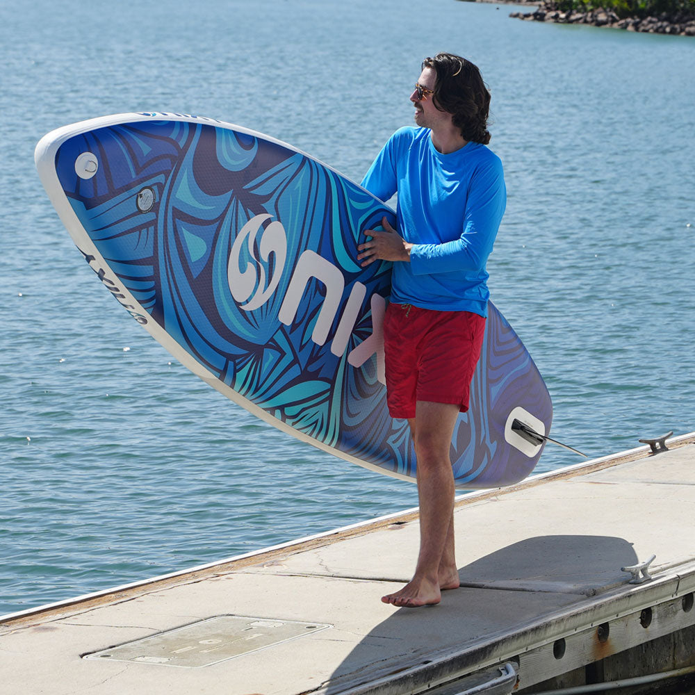 Person holding a blue and white surfboard with a logo on a dock by water