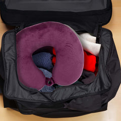 Purple travel neck pillow inside an open black suitcase on a wooden surface