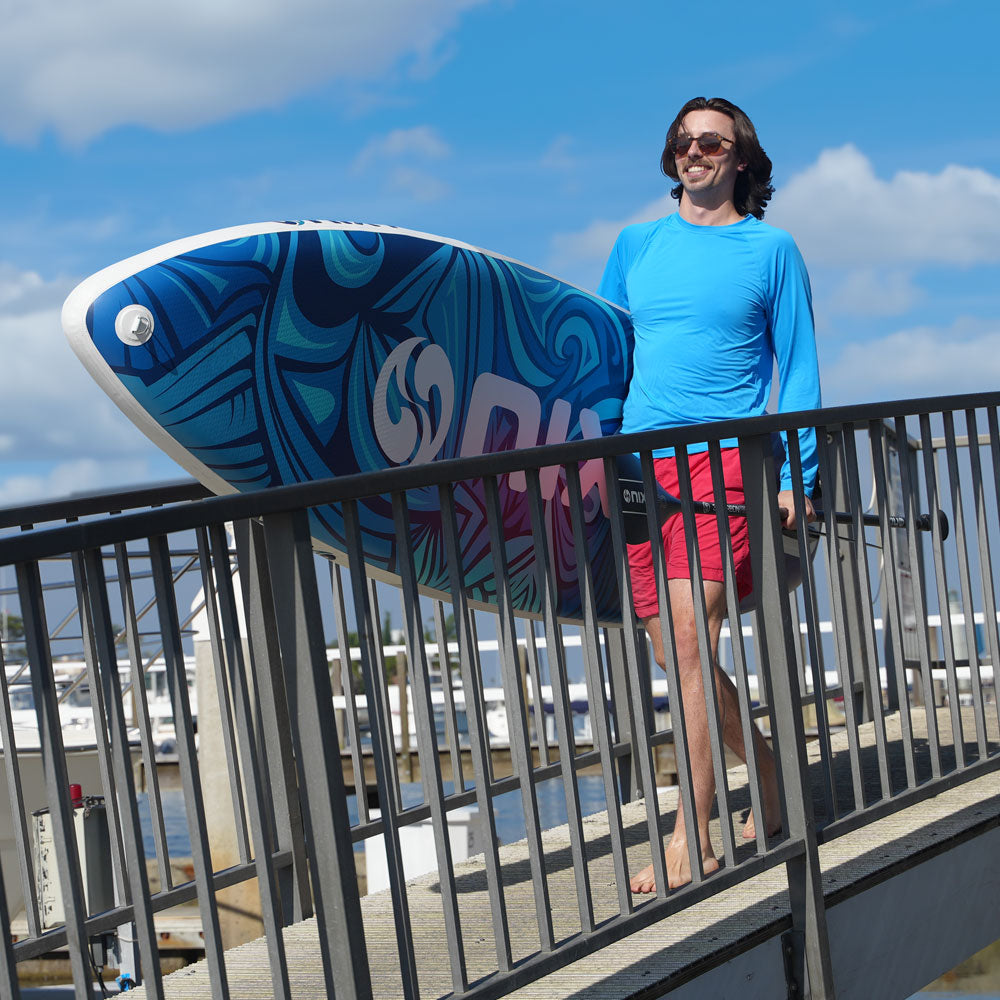 Man holding a blue and white surfboard with a colorful design, standing on a dock.