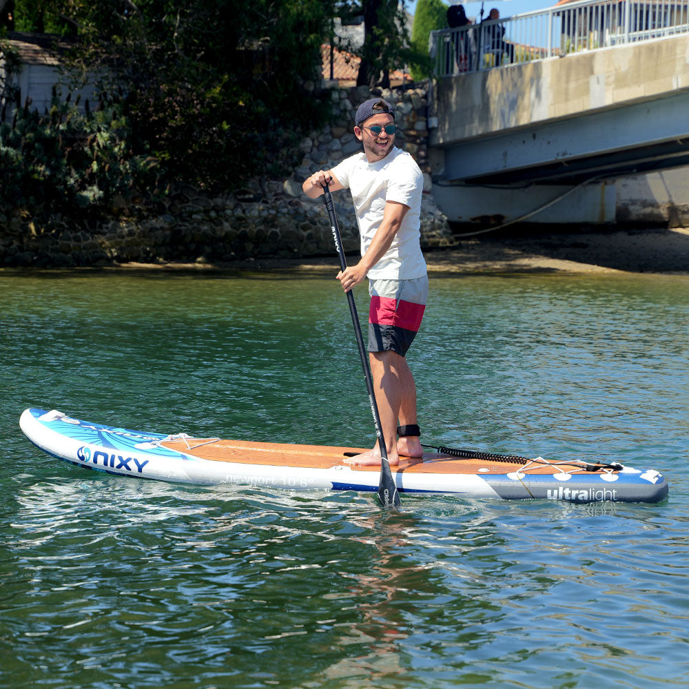 Person paddleboarding on a body of water with a bridge and trees in the background