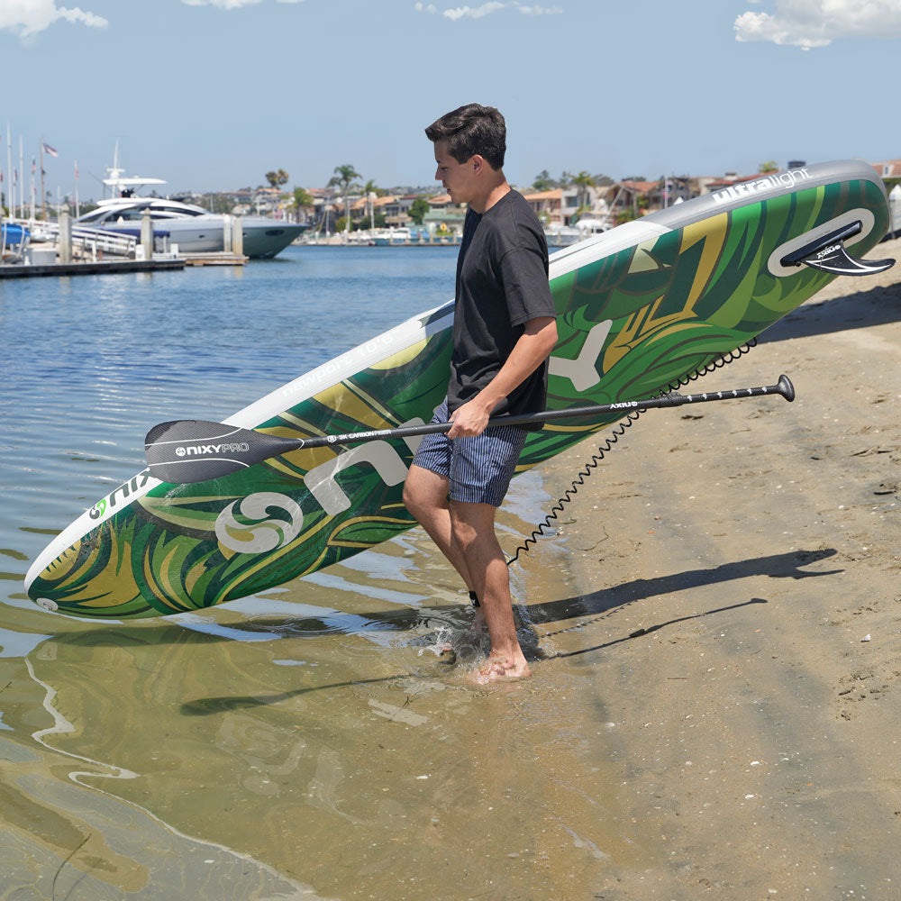 Man carrying a green and white paddleboard with a surfboard design on a dock.