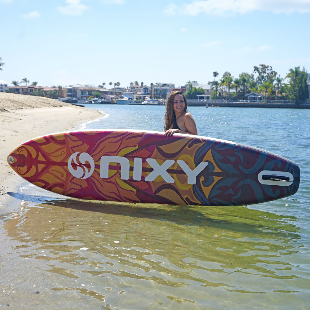 Woman holding a colorful NIXY surfboard on a beach