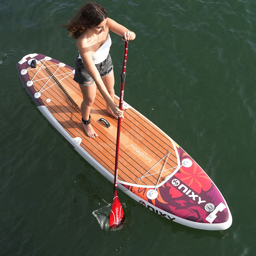 Person paddleboarding on a colorful NIXY board with a red paddle in a body of water.