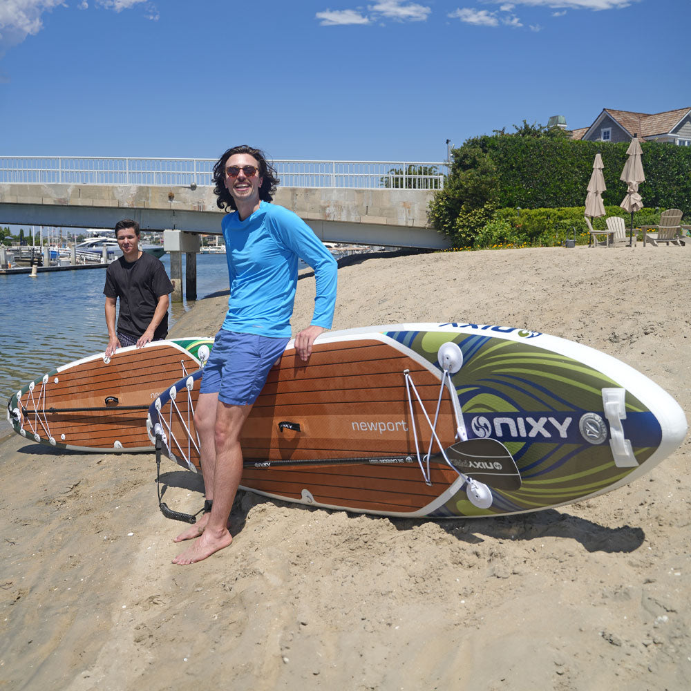 Two people with a NIXY paddleboard on a sandy beach.