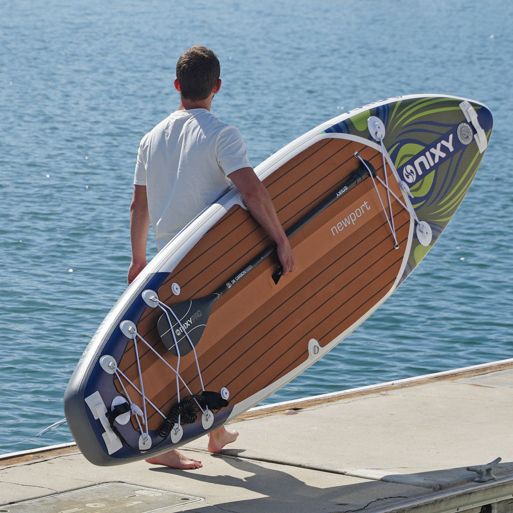 Man holding a large inflatable paddleboard with ONIX branding by the water.