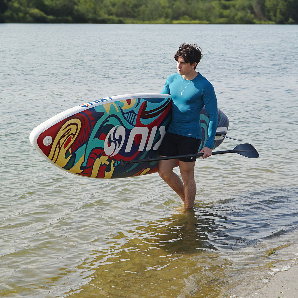 Person holding a colorful paddleboard with a logo in a body of water.