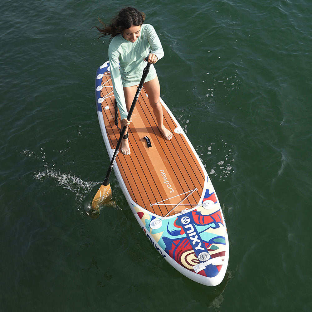 Woman paddleboarding on a colorful board with 'MIXX' branding in a body of water.