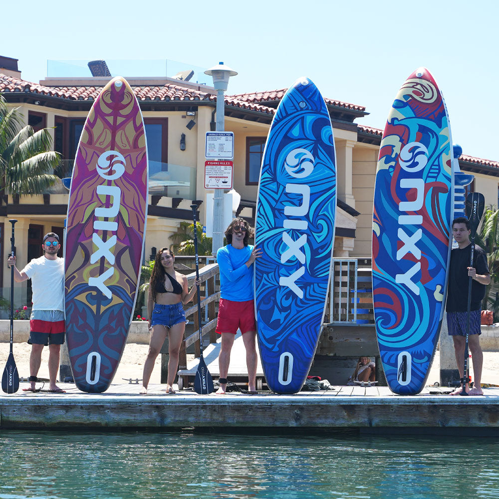 Four people holding colorful surfboards on a dock with a building and palm trees in the background.