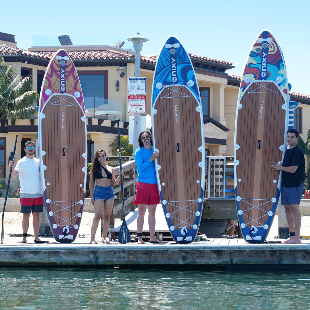 Four people standing on a dock with three colorful surfboards behind them.