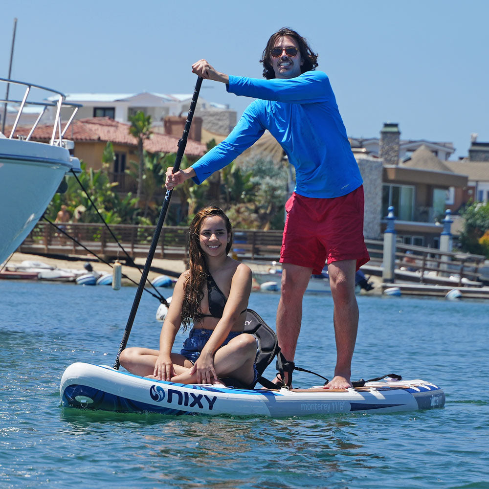 Two people paddleboarding on a NIXY board in a harbor.