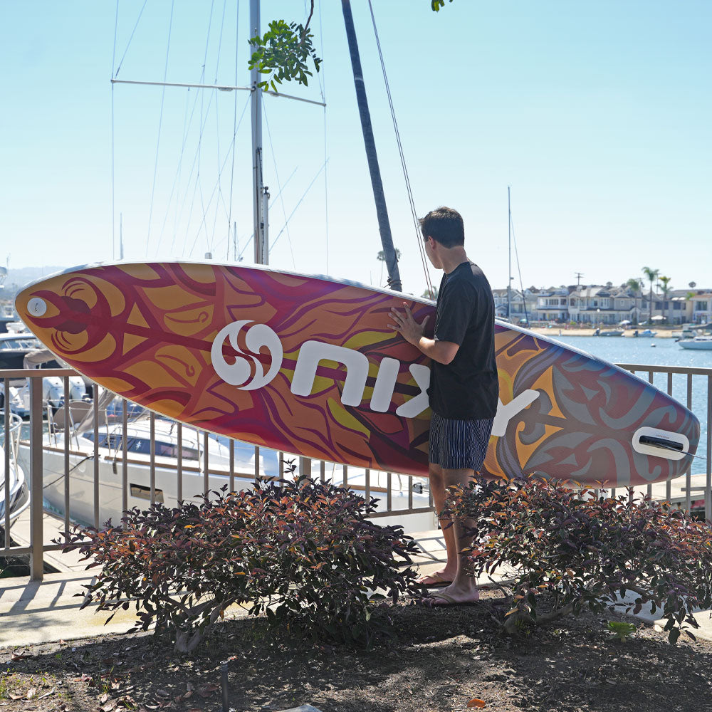 Person holding a colorful surfboard with a marina in the background