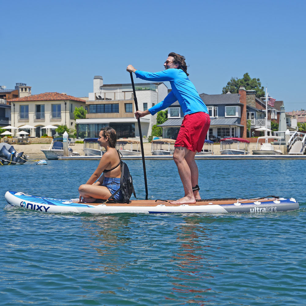 Two people paddleboarding on a calm body of water with houses and boats in the background.