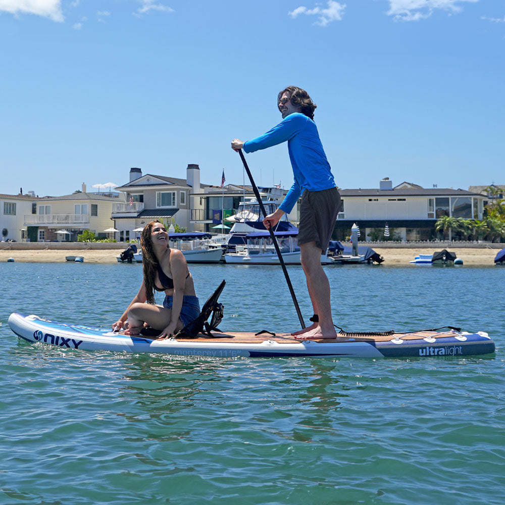 Two people on a stand-up paddleboard in a body of water with buildings in the background.