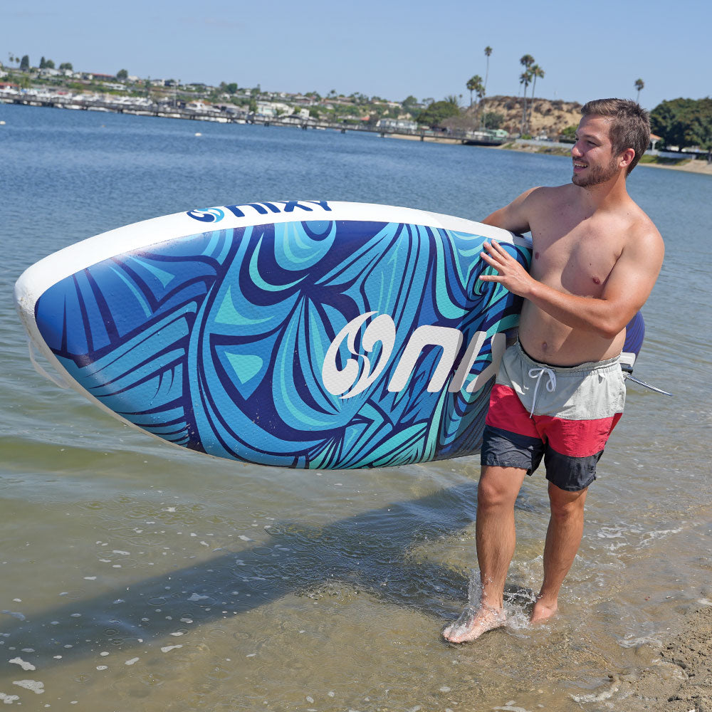 Man holding a blue and white inflatable water board on a beach