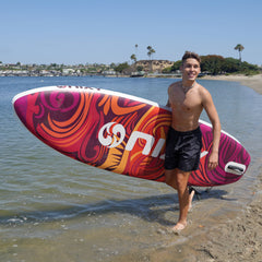 Man holding a colorful surfboard with a beach and water in the background