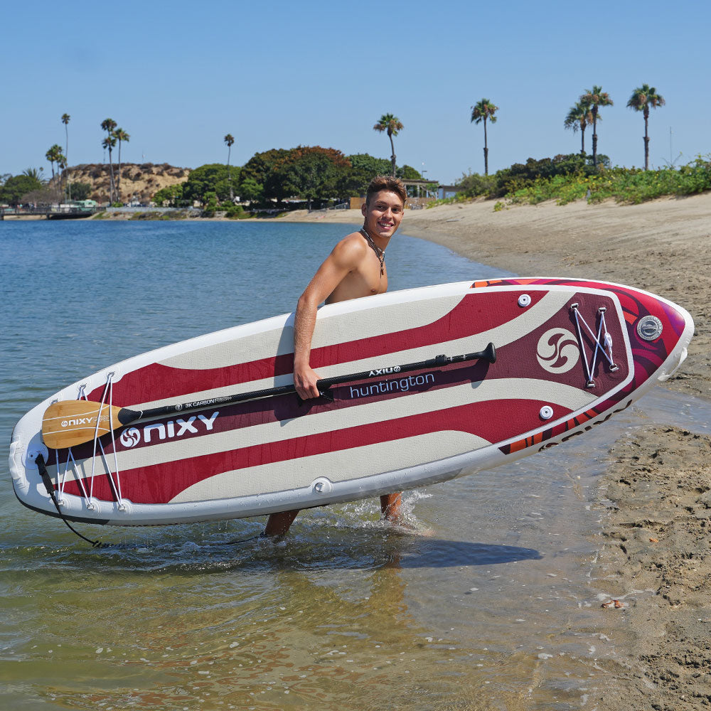 Person holding a red and white paddleboard with palm trees and a clear sky in the background