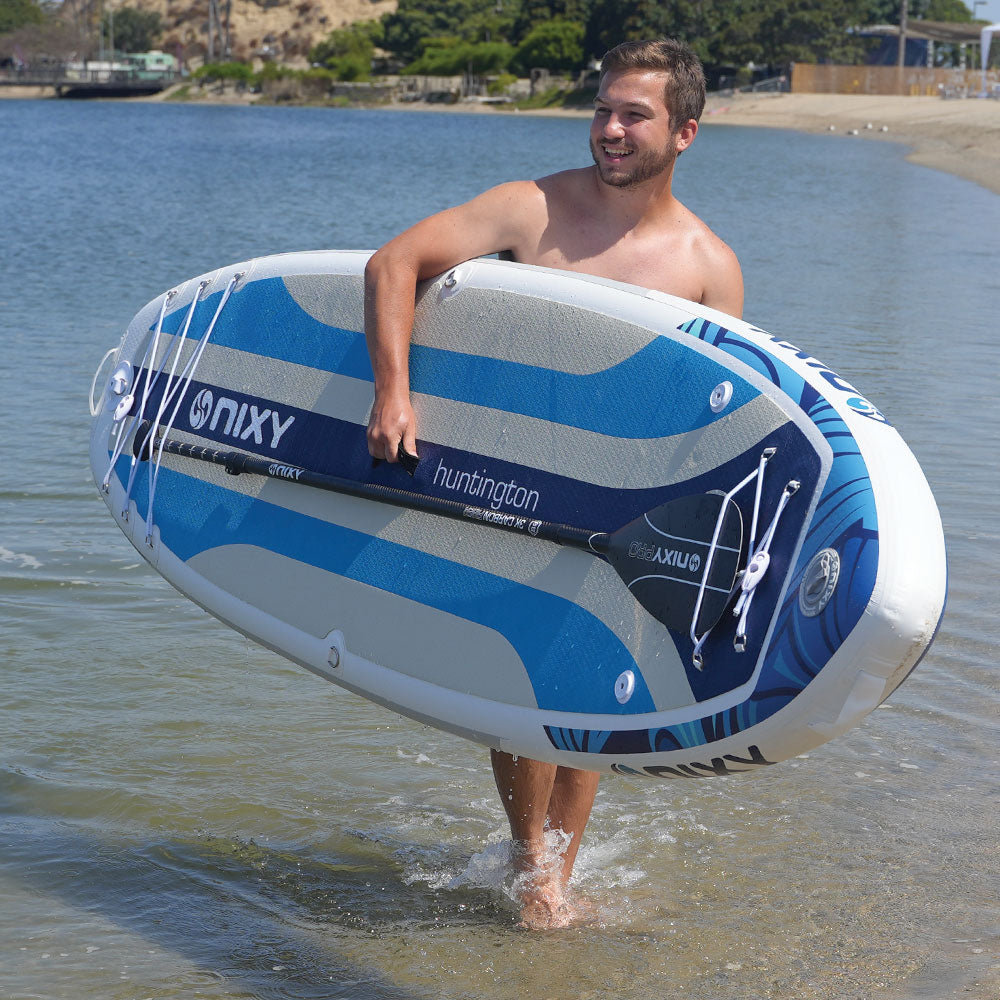 Man carrying an inflatable paddleboard with 'ONIX' branding on a beach.