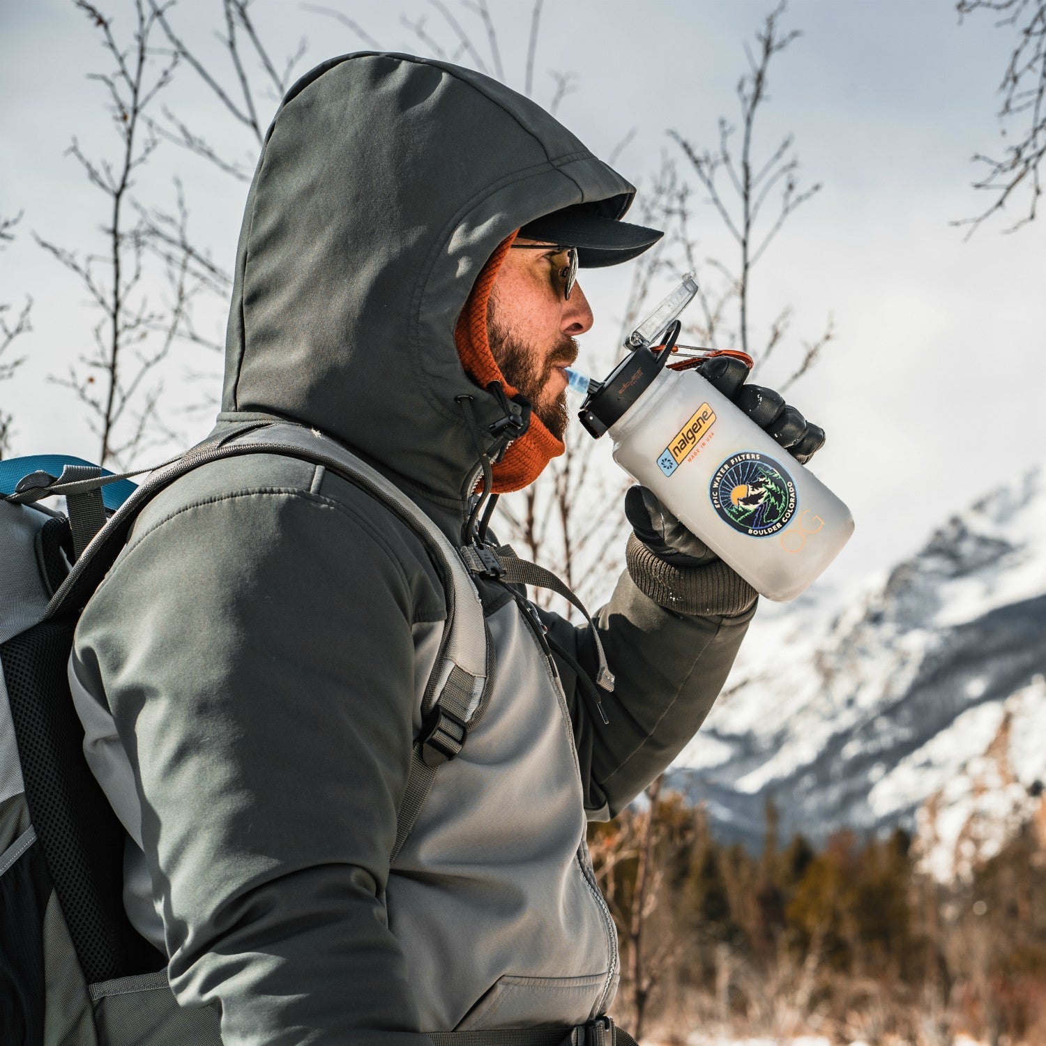 Person in winter clothing drinking from a insulated bottle with mountains in the background
