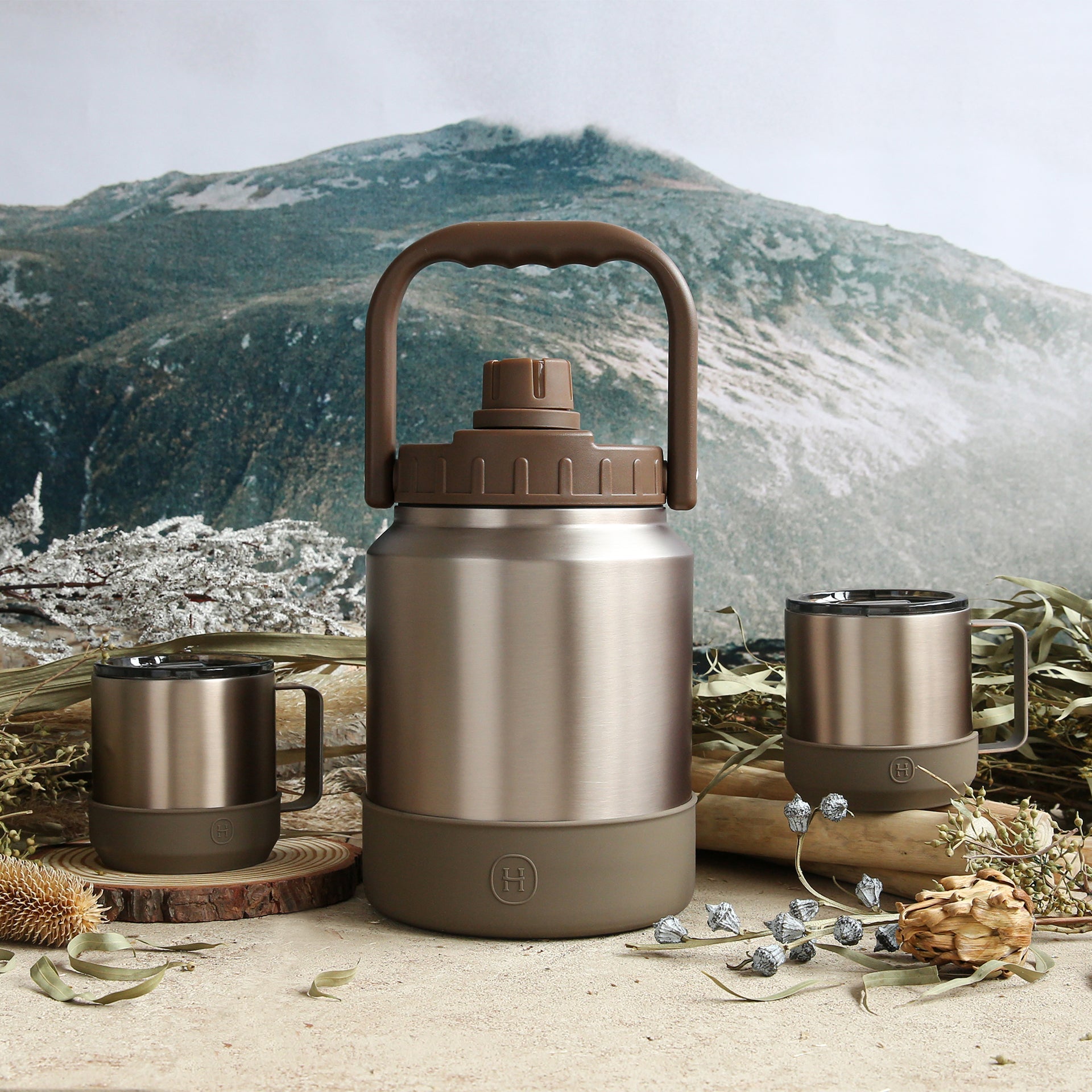 Stainless steel thermos and mugs with a mountainous landscape in the background