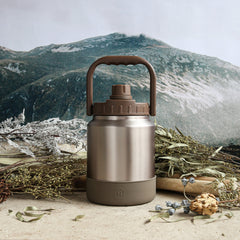 Stainless steel insulated bottle with brown lid on a natural background with mountains.
