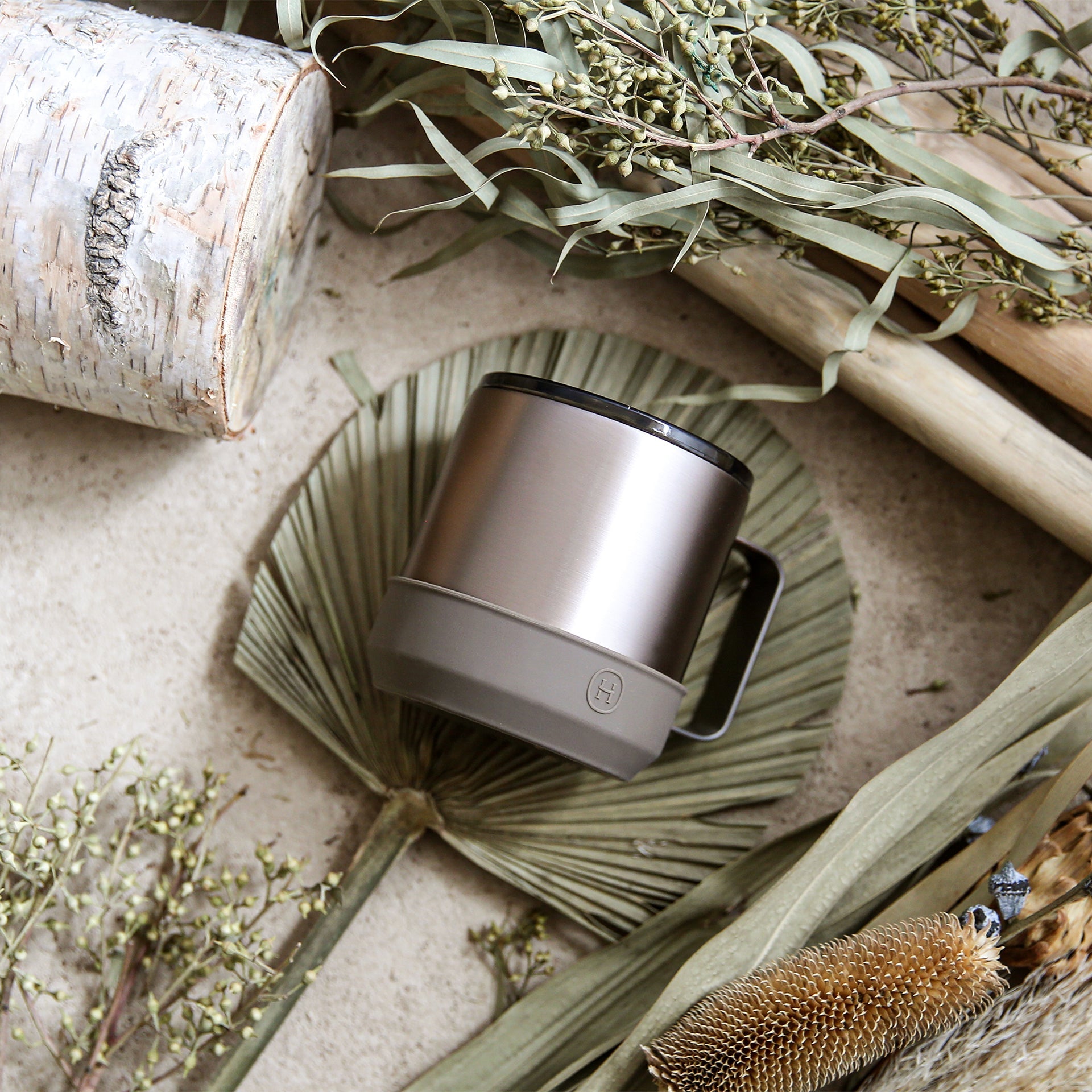 Metallic mug on a textured surface with dried plants and branches