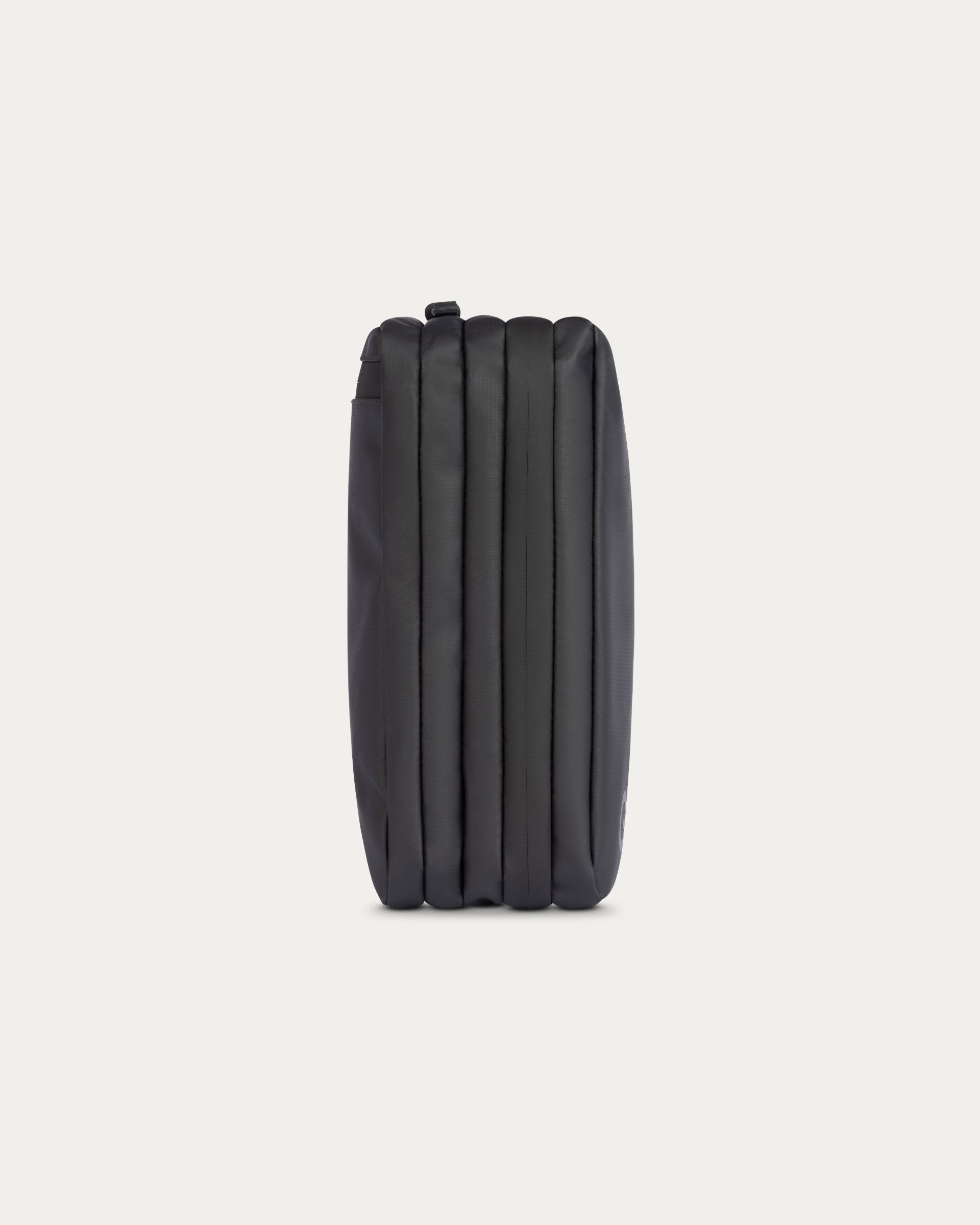 A black zippered pouch with a vertically pleated or ribbed texture, shown from the back against a solid off-white background.