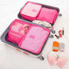 Open suitcase with pink packing cubes and various items on a white background