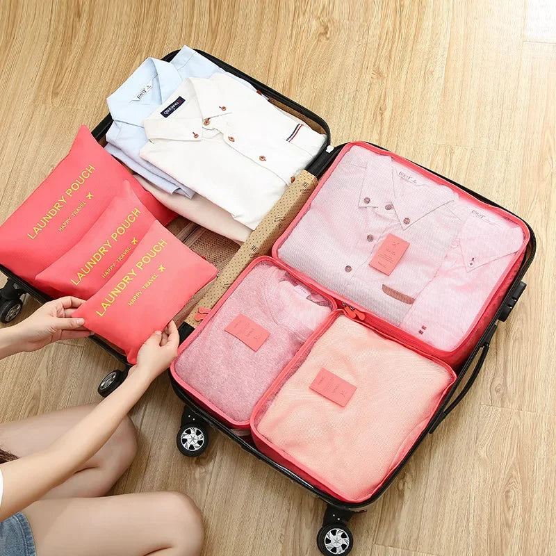 Person organizing pink packing cubes into an open suitcase on a wooden floor.