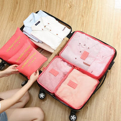 Person organizing pink packing cubes into an open suitcase on a wooden floor.
