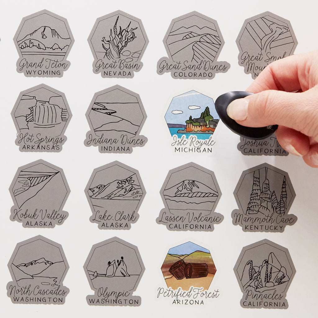 Collection of hexagonal stickers with various national park names and locations, with a hand pressing on one of them.