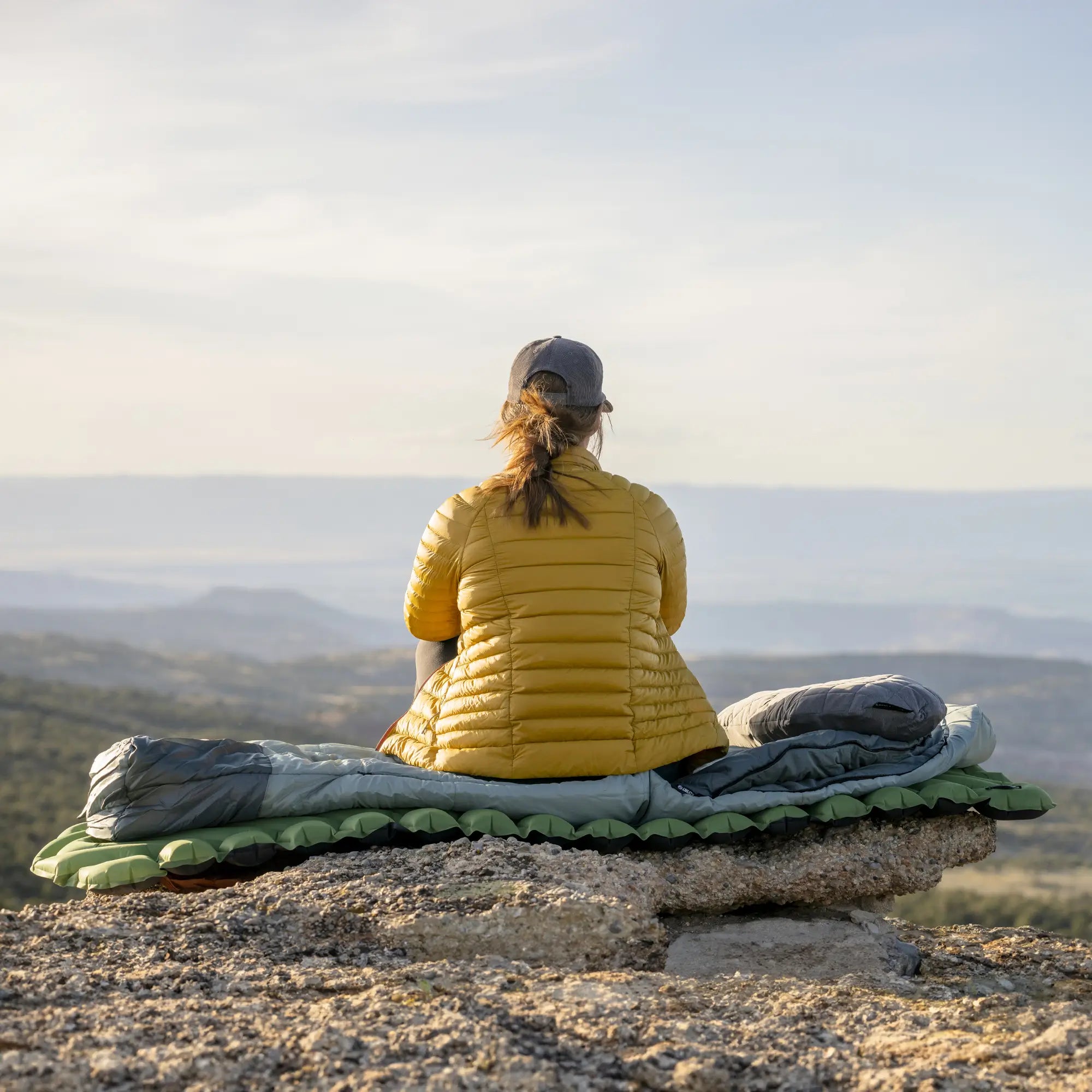 Person in a yellow jacket sitting on a rock with a scenic view