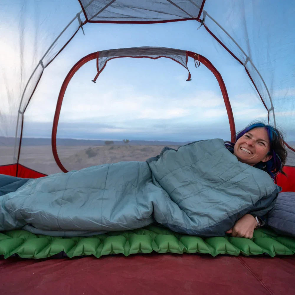 Person lying in a sleeping bag inside a tent with a scenic view outside