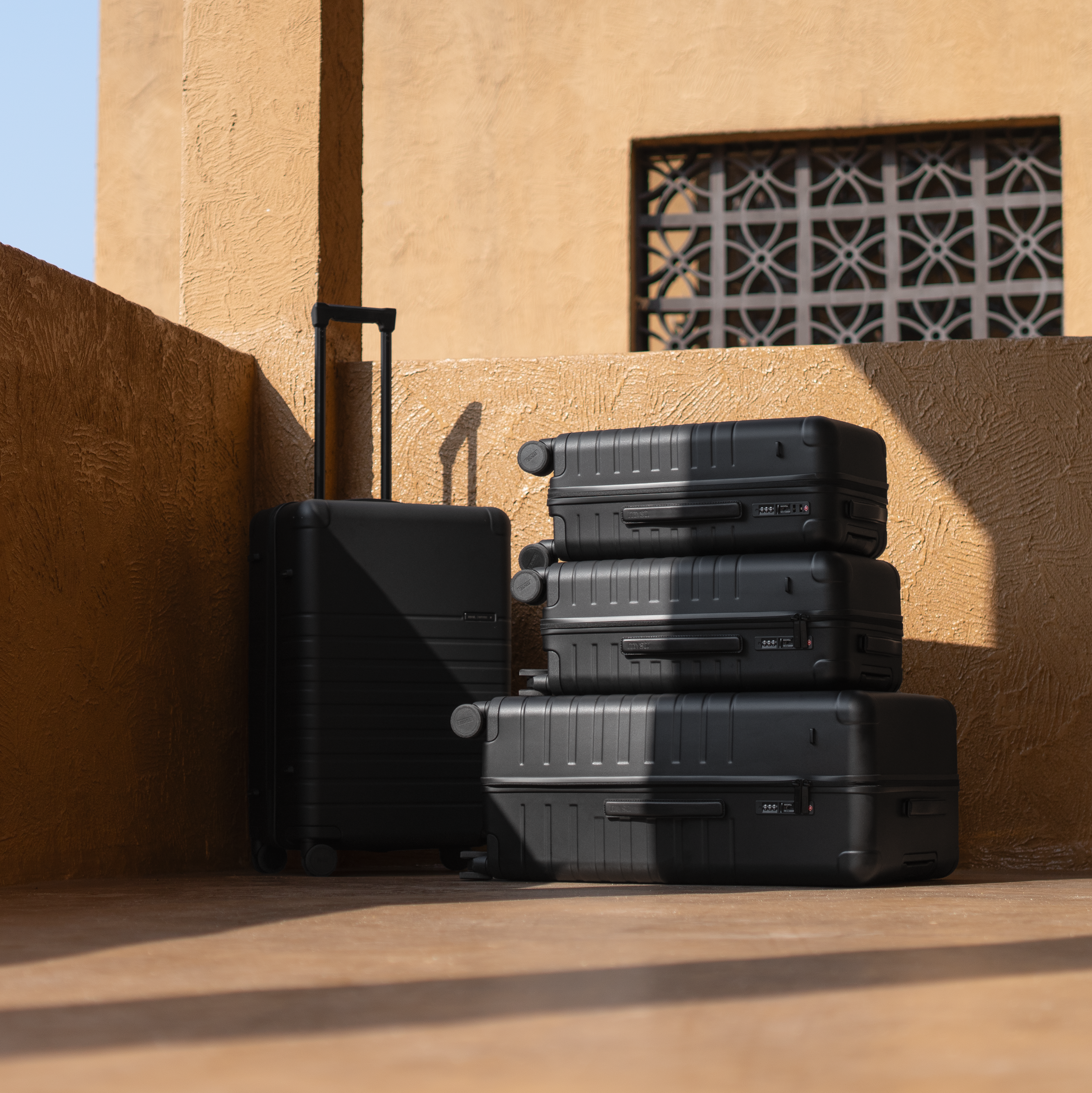 Stack of black suitcases against a beige wall with a window