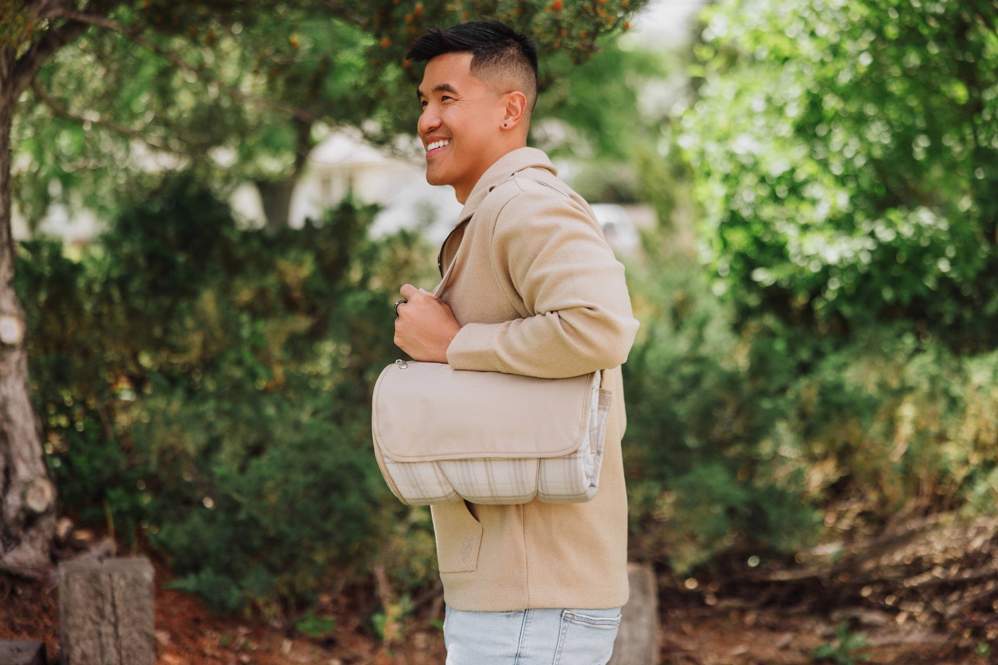 Man holding a beige bag outdoors with greenery in the background