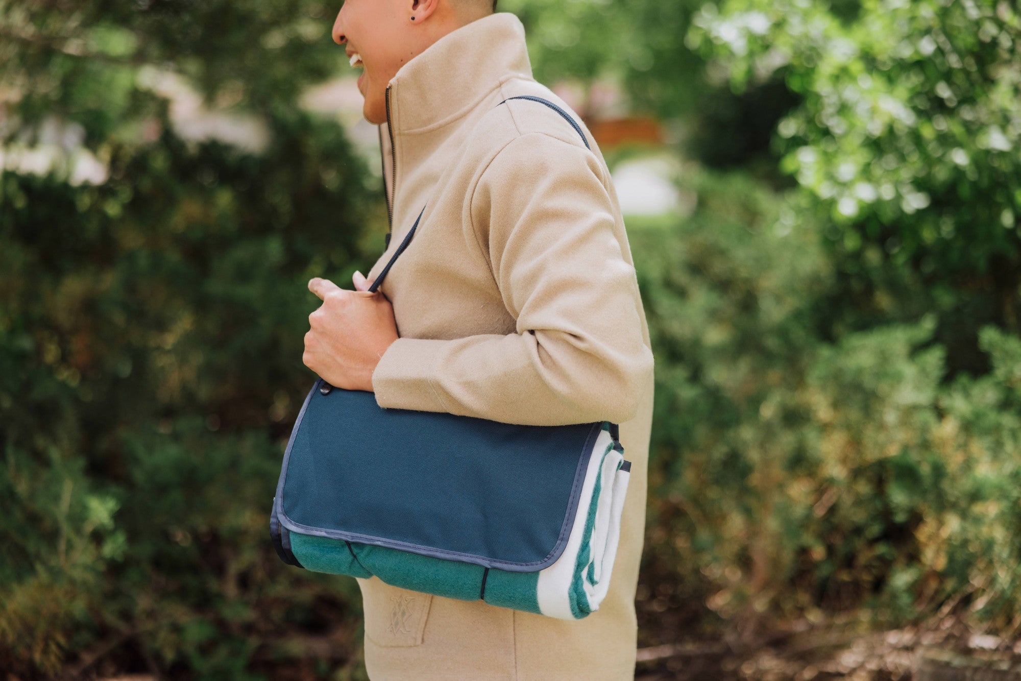 Person holding a blue and green bag outdoors with trees in the background