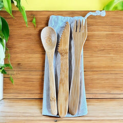 Set of bamboo cutlery including spoon, knife, and fork on a blue cloth with a wooden background.