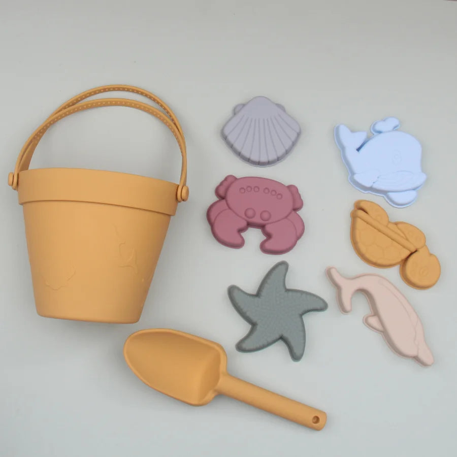 Set of children's sand toys including a bucket, shovel, and sea creature molds on a light gray background.