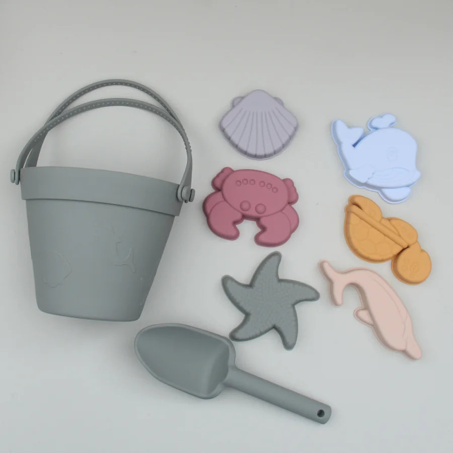 Set of beach-themed toys including a bucket, shovel, and sea creature molds on a light gray background.